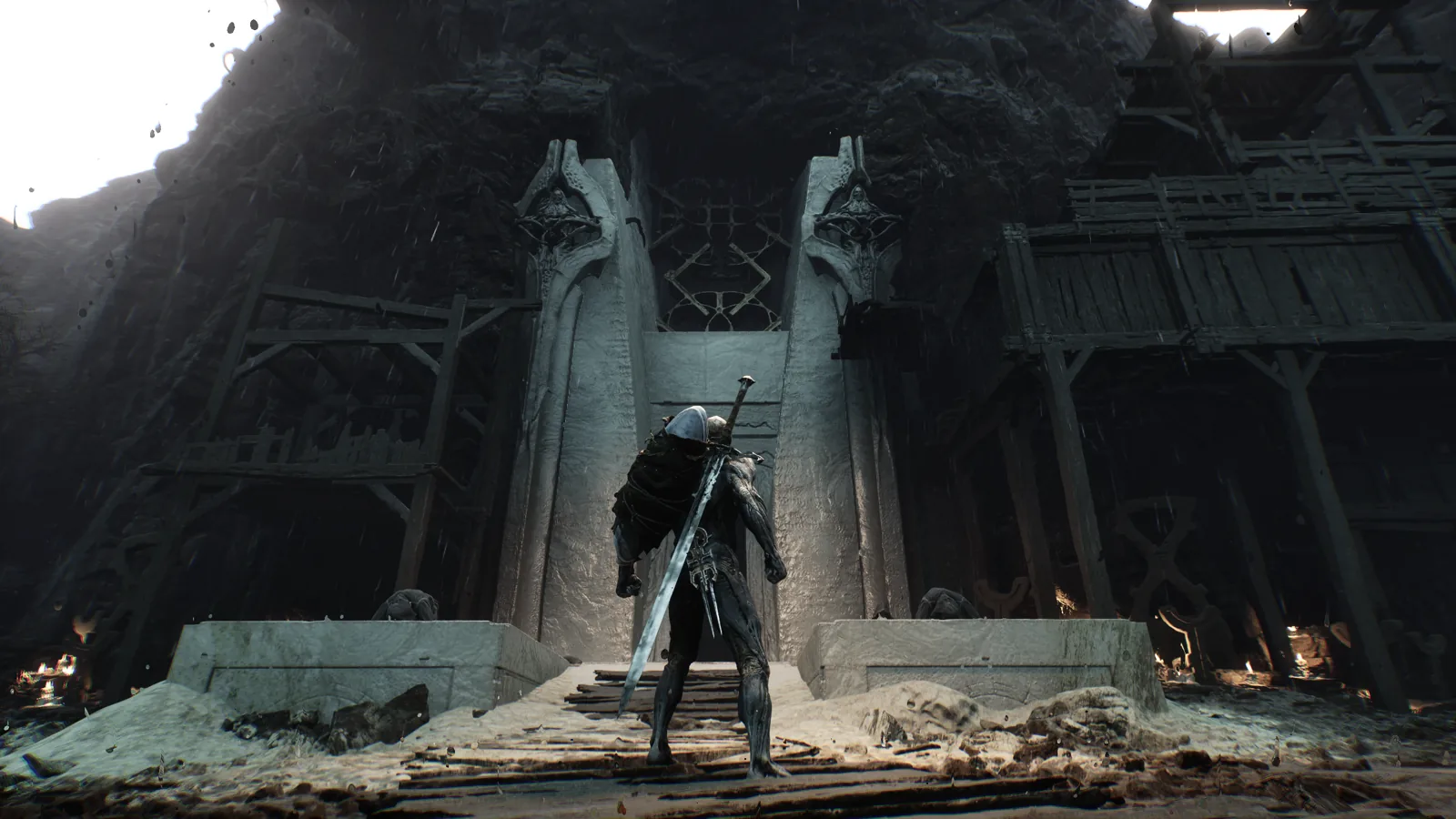 Mortal Shell II screenshot: a hooded warrior with a greatsword on his back stands before towering stone gates carved into a cliff